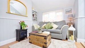A living room with a grey sofa, a wooden chest, a mirror, and a lamp.