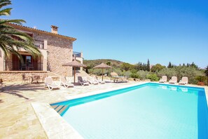 A swimming pool with lounge chairs and umbrellas, surrounded by a stone building with a balcony and a view of trees and hills. - EL COSTER DE NA PLOMERA ( PLOMERA ) - You will love it (Pollensa)
