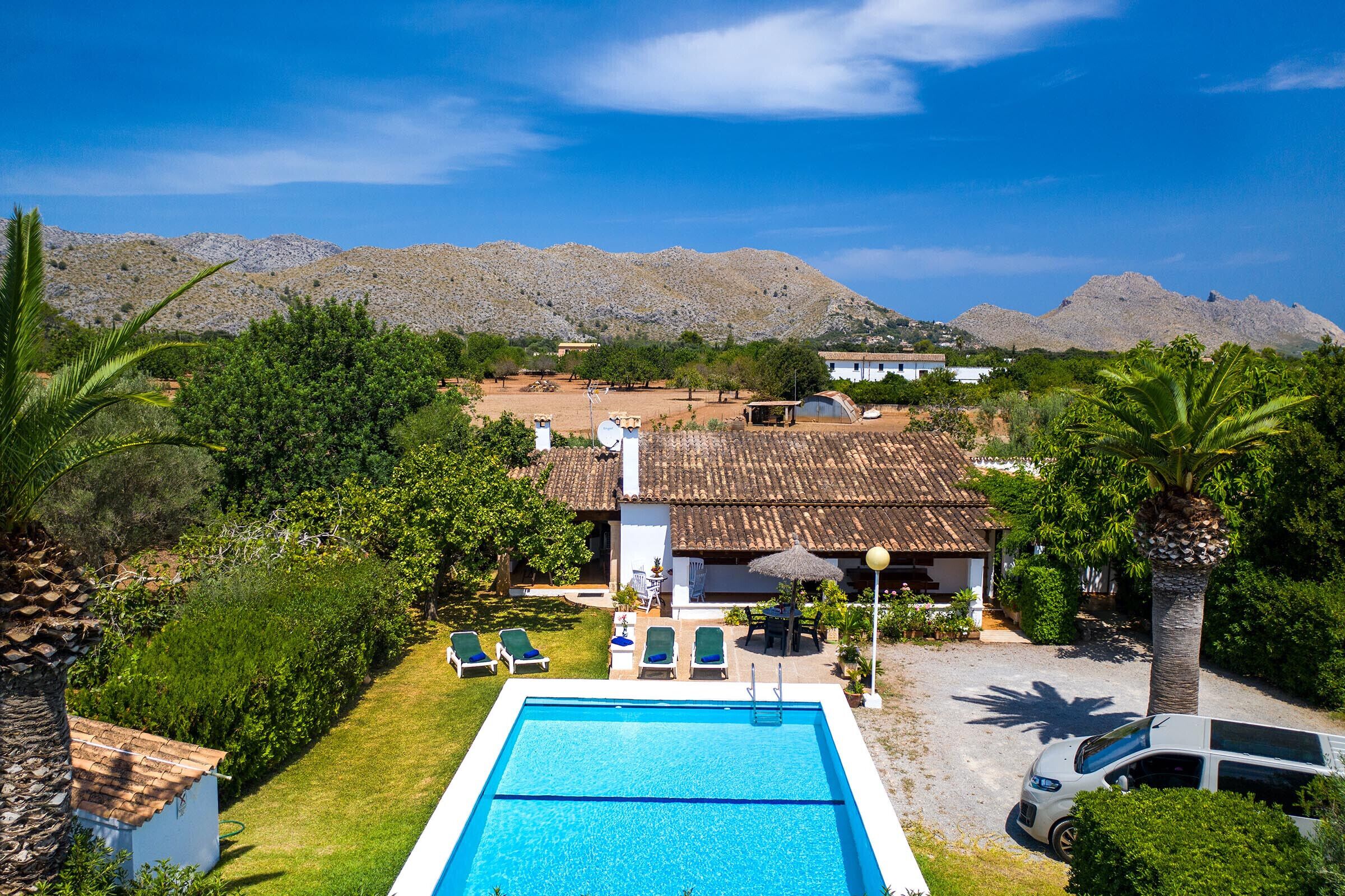 A pool with lounge chairs, a white car, and a house with a tiled roof.