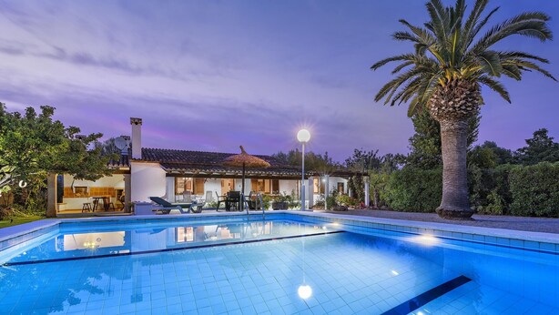 A swimming pool with a tiled deck, a lounge area with chairs and a table, and a palm tree.