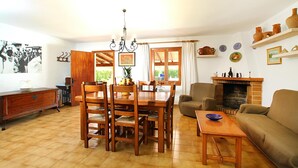 A dining area with a wooden table and chairs, a chandelier, and a fireplace.