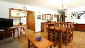 A spacious living area with a wooden dining table, a television, and a kitchen area with wooden cabinets and a countertop.