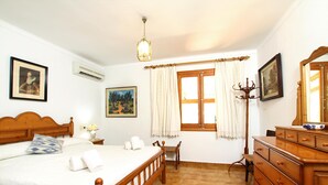 A bedroom with a wooden bed, a nightstand, a dresser, a chair, a window with curtains, and a hanging lamp.