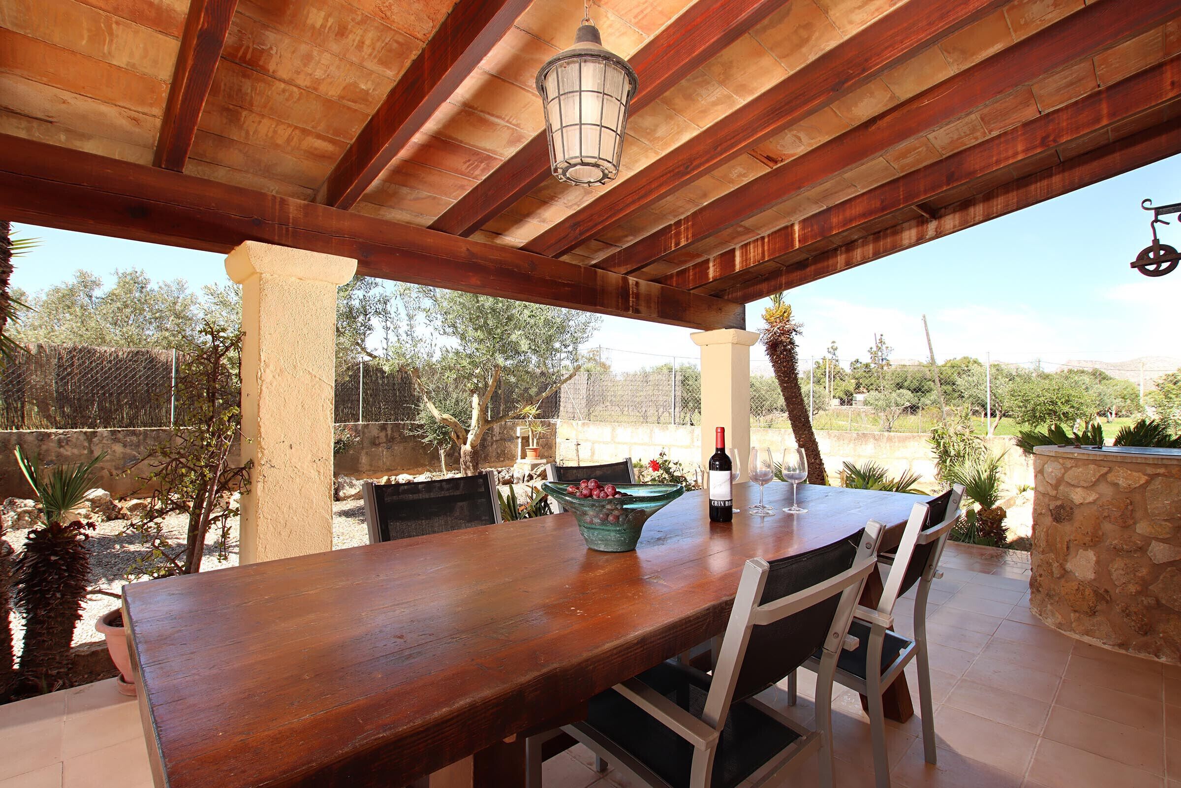 Une terrasse extérieure avec une table en bois, des chaises, un luminaire suspendu et une vue sur le paysage environnant.