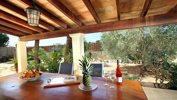 An outdoor dining area with a wooden table, a pineapple centerpiece, wine glasses, and a bottle. - L´Embat ( Tolo ) Charming 2 bedroom villa (Pollensa)