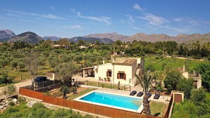 A villa with a swimming pool, surrounded by a fenced yard and mountains in the background. - L´Embat ( Tolo ) Charming 2 bedroom villa (Pollensa)