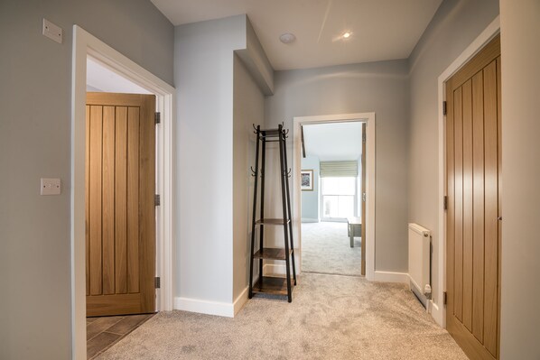 A hallway with wooden doors, a coat rack, and a carpeted floor.
