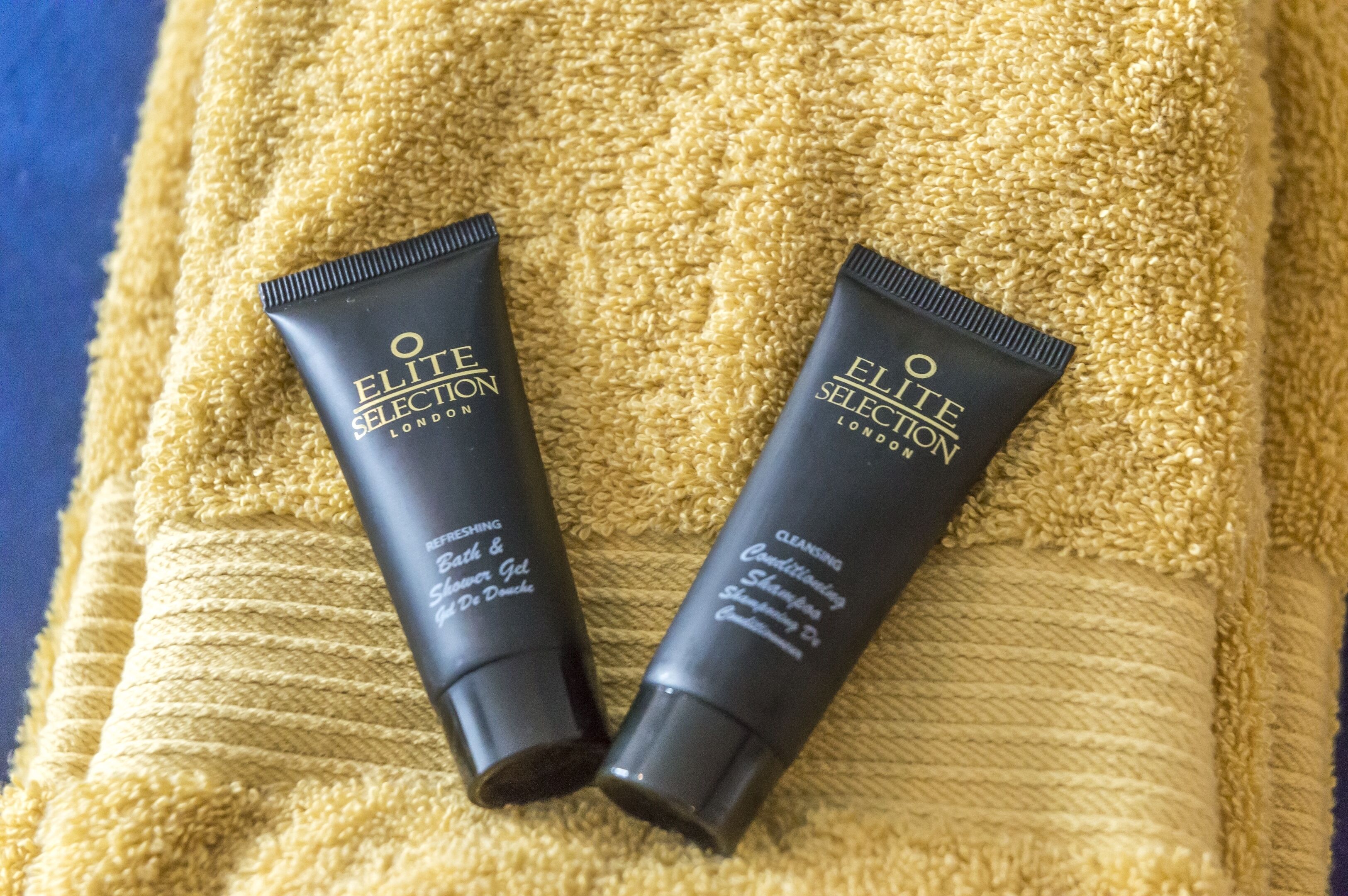 Two tubes of Elite Selection London cleansing shampoo and conditioner on a yellow towel.