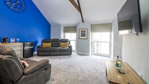 Un salon moderne avec un mur d’accent bleu, un canapé en cuir, un fauteuil inclinable, une table basse, un téléviseur à écran plat et un réfrigérateur.