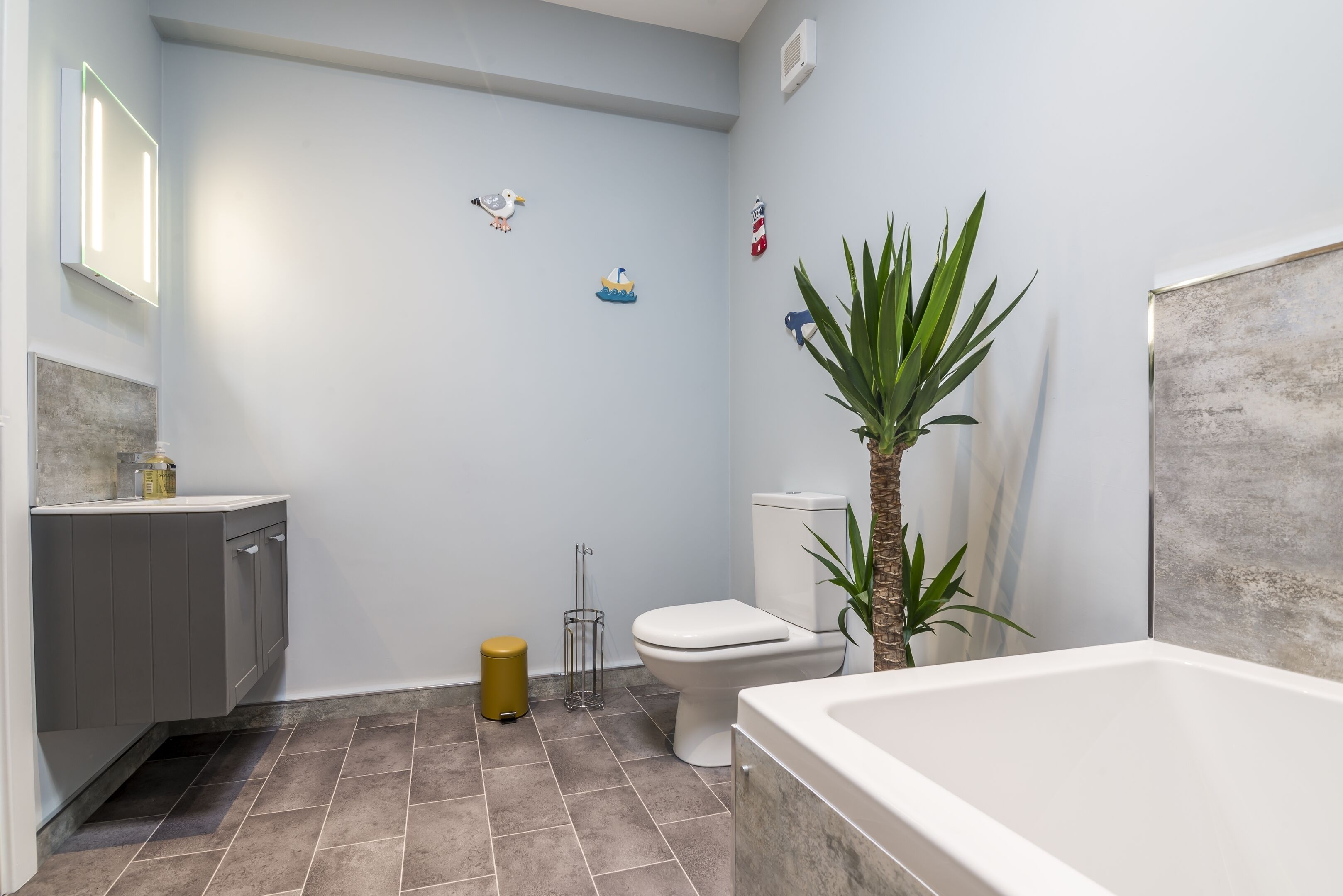 Un baño con bañera, inodoro, lavabo y una planta en maceta.