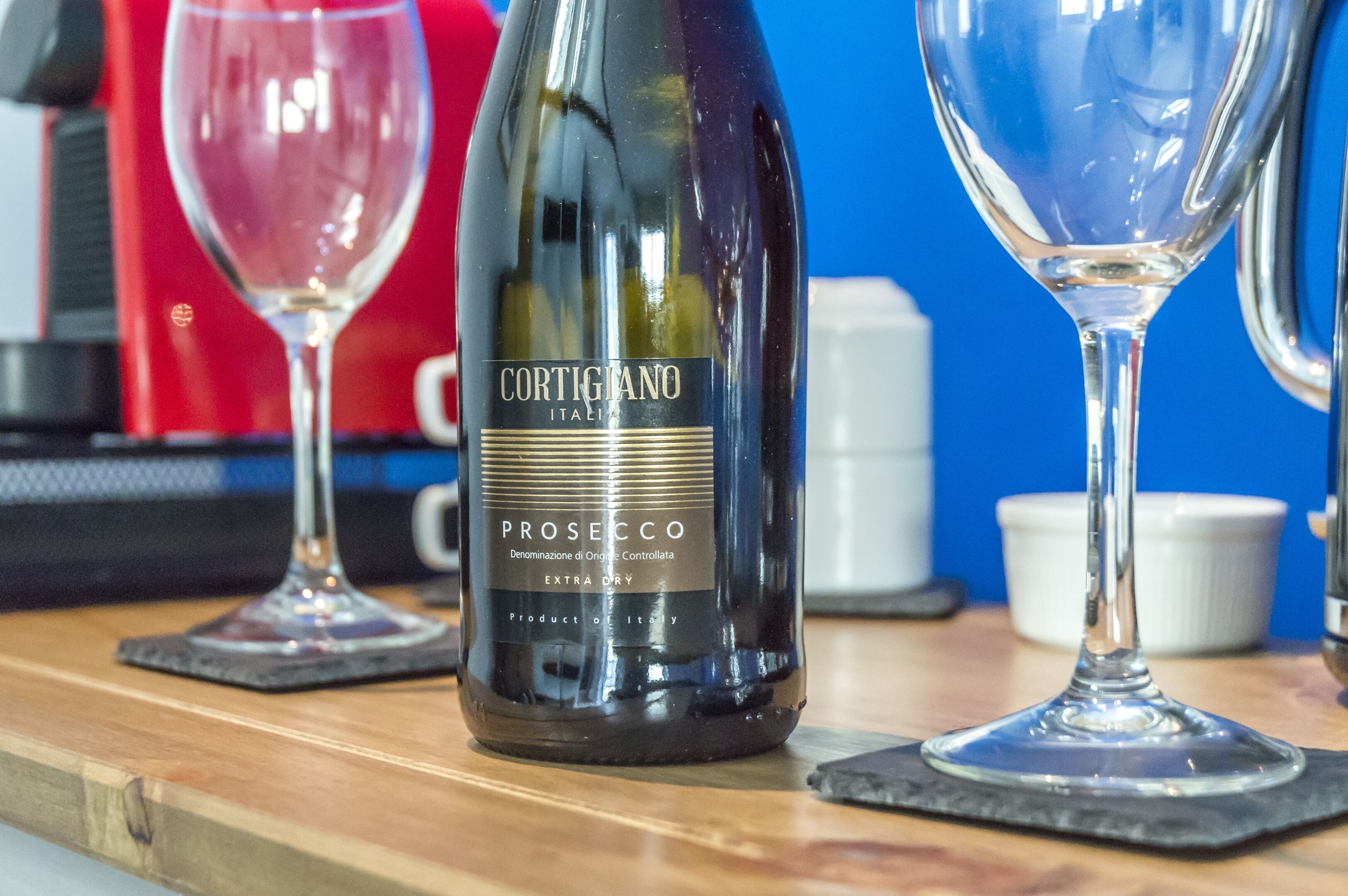 A bottle of Cortigiano Prosecco wine on a wooden table with two wine glasses.