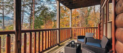 A wooden deck with wicker furniture and a view of autumn trees.
