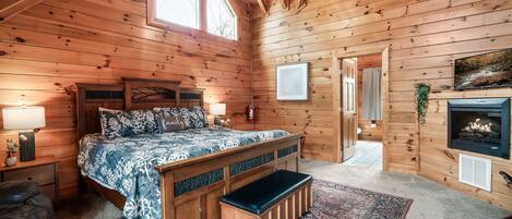 Ein Schlafzimmer einer Holzhütte mit Bett, Bank, Nachttischen und Kamin.