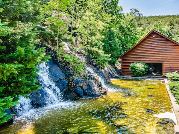 Una cabaña de madera con cascada y estanque.