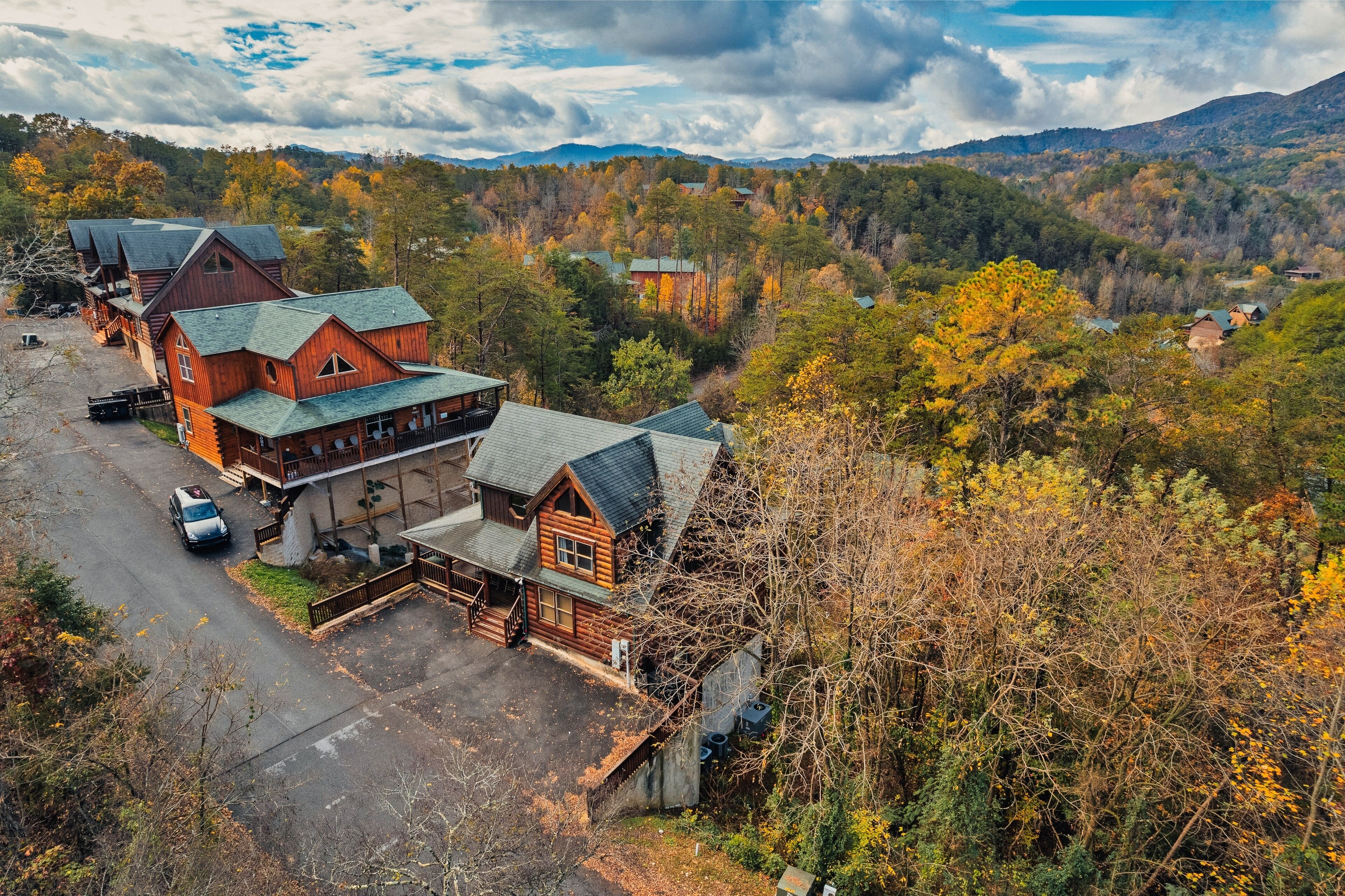 Un hôtel aménagé dans un chalet en rondins, composé de plusieurs bâtiments, avec un espace de stationnement et un paysage montagneux en toile de fond.