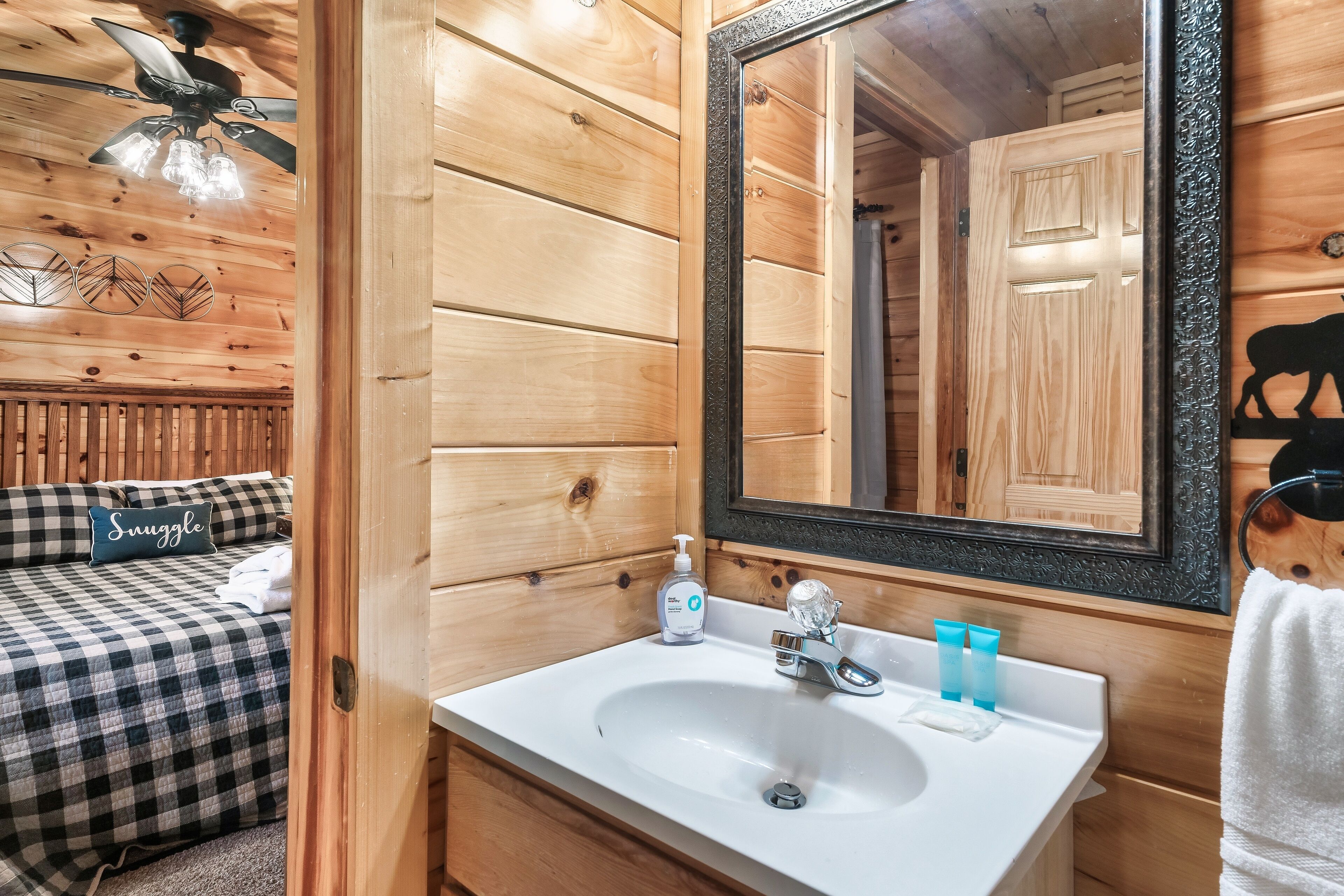 A wooden cabin interior with a bed, a white sink, a mirror, and a ceiling fan.