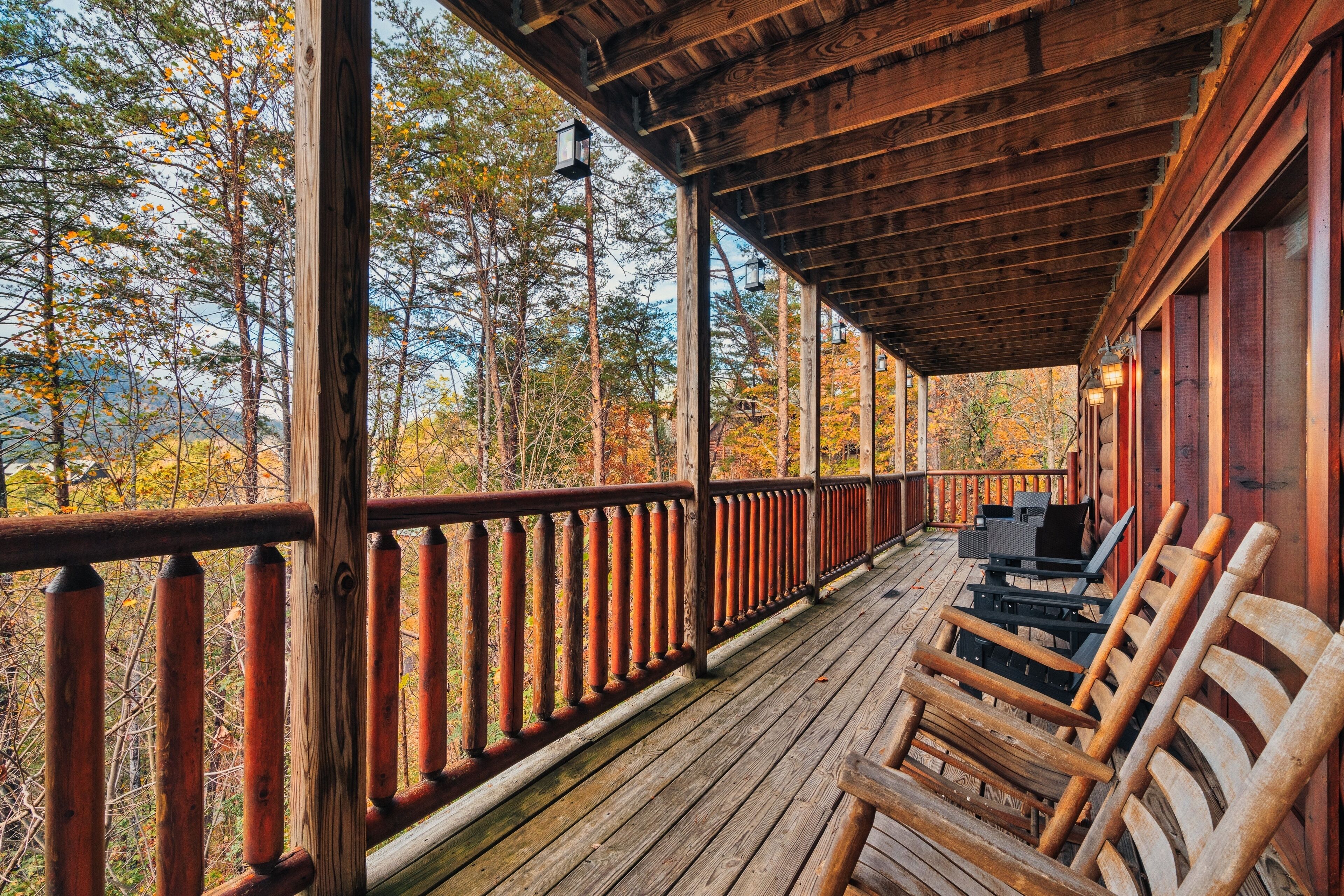 A wooden deck with a railing, outdoor furniture, and a view of trees.