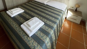 Ein ordentlich bezogenes Bett mit einem gemusterten Überwurf, ein Nachttisch mit Lampe und ein Kleiderschrank in einem Hotelzimmer.