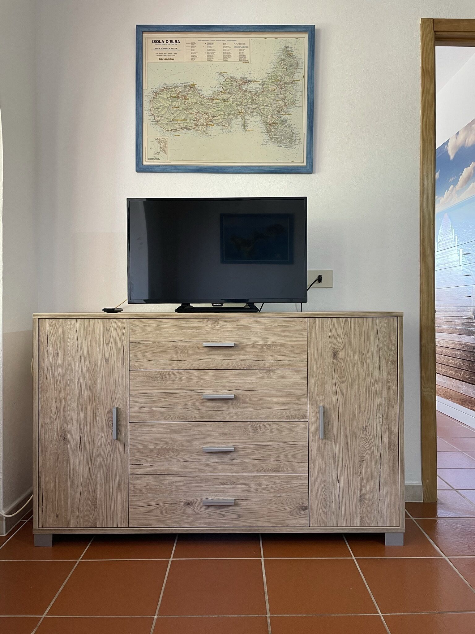 A wooden cabinet with drawers, a television on top, and a framed map on the wall.