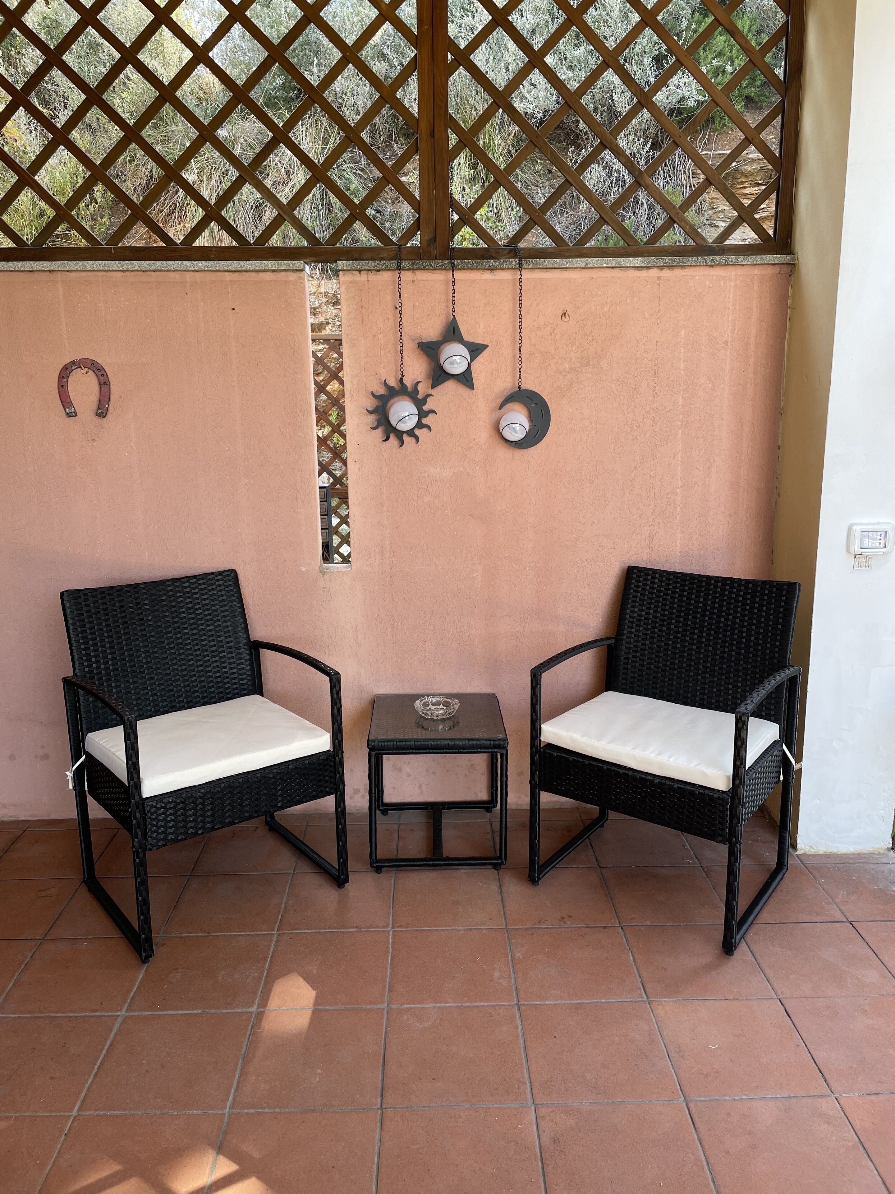 A patio area with two wicker chairs, a small table, and decorative wall elements including a horseshoe and sun/moon motifs.