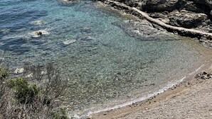 Eine felsige Küste mit klarem Wasser, einem Sandstrand und fernen Bergen.