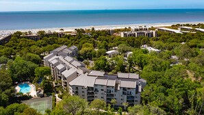 A multi-story hotel with a pool, surrounded by dense greenery and a beach in the background. - Sunny Coastal Villa| Private Decks, Pool, Tennis | Near Dining & Scenic Grounds (Hilton Head Island)