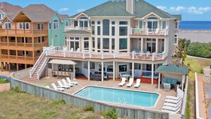 A large, multi-story house with a pool, outdoor seating, and a view of the ocean. - Premier Oceanfront Dog Friendly w/ Pool, Elevator, Hot Tub, Theater, Game Room (Hatteras)