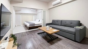 Um espaço de estar moderno e compacto, com sofá, mesa pequena, cama e televisão.