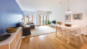 Una sala de estar moderna con un sofá, una mesa de comedor con sillas, una lámpara y un ventanal grande.