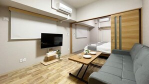 Habitación de hotel pequeña con televisión de pantalla plana, una cama, un sofá y una mesita con una planta y una taza.