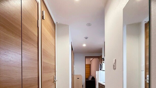 Un pasillo con suelo de madera, un espejo a la derecha y una puerta a la izquierda.