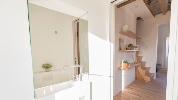 A modern bathroom with a large mirror, white sink, and wooden staircase leading to a loft area. - Historial Apartment Santos IV (Lisboa)