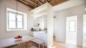 A modern kitchen with white cabinetry, a wooden dining table, and a bowl of fruit. - Historial Apartment Santos IV (Lisboa)