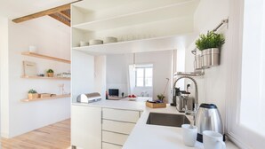 A modern kitchen with white cabinetry, wooden shelves, and a built-in stove. - Historial Apartment Santos IV (Lisboa)