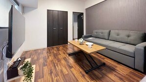 Un salon moderne avec un canapé gris, une table basse en bois et un téléviseur placé à gauche.
