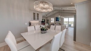 A modern kitchen with white cabinetry, a large island, and a dining area with white chairs and a chandelier.