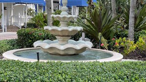 Un edificio bianco con persiane blu e il numero '1883' sulla facciata, circondato da vegetazione rigogliosa e una fontana centrale.