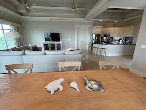 A spacious living room with a large sofa, a wooden dining table with a turtle sculpture, and a kitchen area with modern appliances.