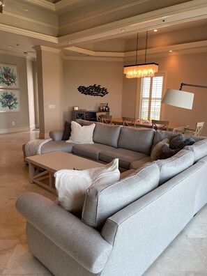 A spacious living room with a large grey sectional sofa, a wooden coffee table, and a dining area with a table and chairs.
