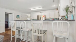 Eine Küche mit weißen Schränken, einem Edelstahlkühlschrank und einer Bar mit weißen Stühlen.