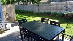Une terrasse avec une table et des chaises, un hamac et une clôture en bois en arrière-plan.