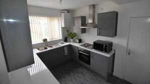 A compact kitchen with a sink, stove, microwave, and cabinets. - Beautiful 3-bed House in Wolverhampton (Wolverhampton)