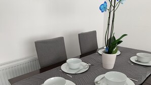 A dining table set with white plates, bowls, and cutlery, flanked by grey upholstered chairs. - Beautiful 3-bed House in Wolverhampton (Wolverhampton)