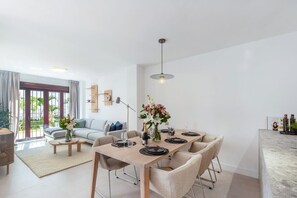 A modern living room with a dining area, a sofa, a coffee table, and a kitchen counter. - La Maestranza | Puerto Banus Townhouse Bbq Pool (Marbella)