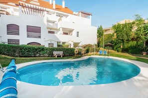 A swimming pool with a clear blue water, a white building with balconies, and a well-maintained garden. - La Maestranza | Puerto Banus Townhouse Bbq Pool (Marbella)