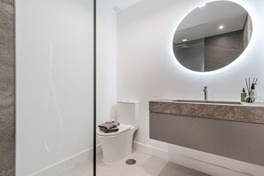 A modern bathroom with a glass shower enclosure, a toilet, a sink with a marble countertop, and a round mirror. - La Maestranza | Puerto Banus Townhouse Bbq Pool (Marbella)