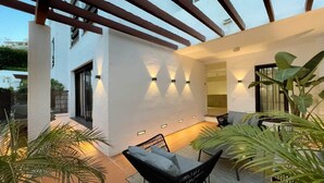A modern outdoor patio with a black wicker chair, a small table, and wall-mounted lights.