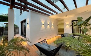 A modern outdoor patio with a black wicker chair, a small table, and wall-mounted lights. - La Maestranza | Puerto Banus Townhouse Bbq Pool (Marbella)