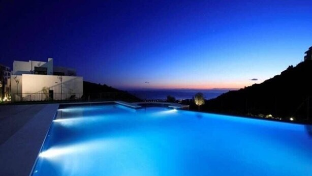 A swimming pool at dusk with a view of the ocean and a modern building in the background. - Samara 2 | Marbella Luxury Spa Gym Pools Views (Marbella)