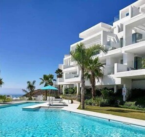 A modern hotel with a pool, white exterior, and palm trees.